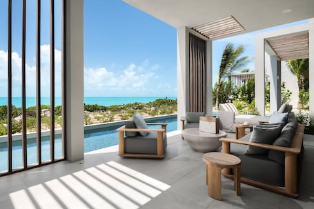A modern outdoor lounge area with a pool, seating, and a view of the ocean.