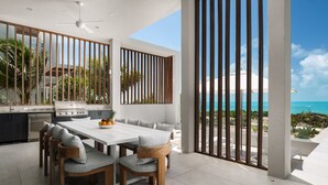 A modern kitchen with a large island, white cabinetry, and a view of the ocean. - Ocean Estate Banks 5 Bedroom OE14 (Providenciales)