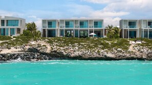 Ein Hotel direkt am Strand mit mehrstöckigen Gebäuden, Balkonen und freiem Blick auf das türkisfarbene Meer.