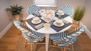 Una mesa de comedor redonda con cubierta blanca, rodeada por cuatro sillas de estampado azul y blanco. La mesa está servida con platos, tazones y vasos.
