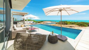 Zona de piscina con asientos al aire libre, sombrillas y vista al océano.