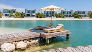 Un moderno resort con terraza de madera, sillas de descanso y vista despejada al océano.