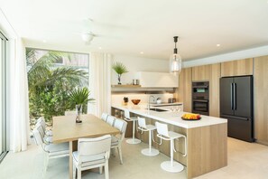 Een moderne keuken met een centraal eiland, witte barkrukken en een grote koelkast.