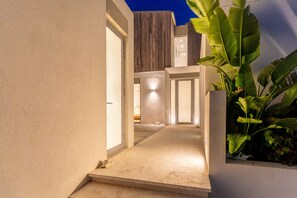 A narrow hallway with a concrete floor leading to a room with a bed. - Lagoon Villa 6 Bedrooms Including Guesthouse LV03 (Providenciales)