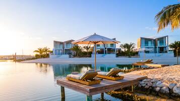 A modern resort with a pool, lounge chairs, and a wooden deck over water.