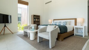 Une chambre moderne comprenant un lit, deux fauteuils, une table d’appoint, une bibliothèque et un téléviseur.