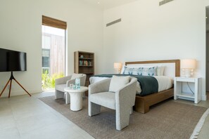 Ein modernes Schlafzimmer mit einem Bett, zwei Sessel, einem Beistelltisch, einem Bücherregal und einem Fernseher.