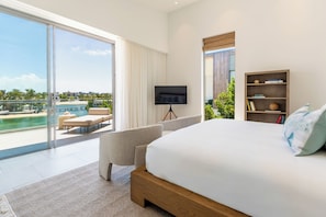 Un dormitorio con una cama grande, televisor, estantería y vista a una piscina y edificios.