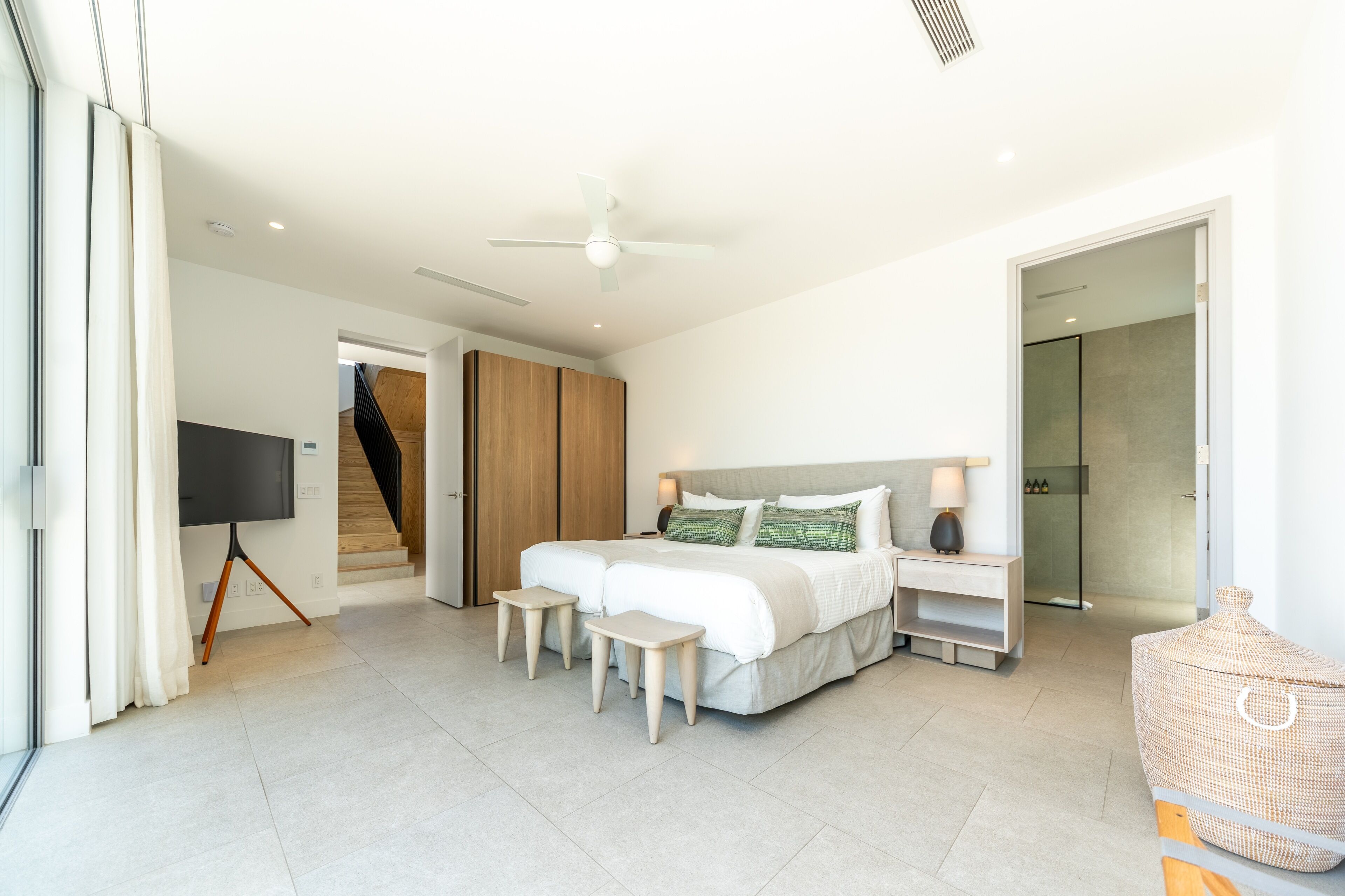 A modern bedroom with a large bed, bedside tables, a TV, and a staircase leading to another room.
