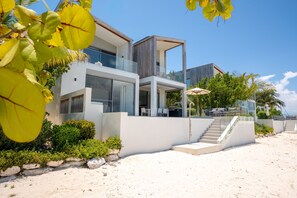 Ein modernes Strandgrundstück mit einer zweistöckigen Struktur, einem gläsernen Balkon und einer Treppe, die zum Obergeschoss führt.