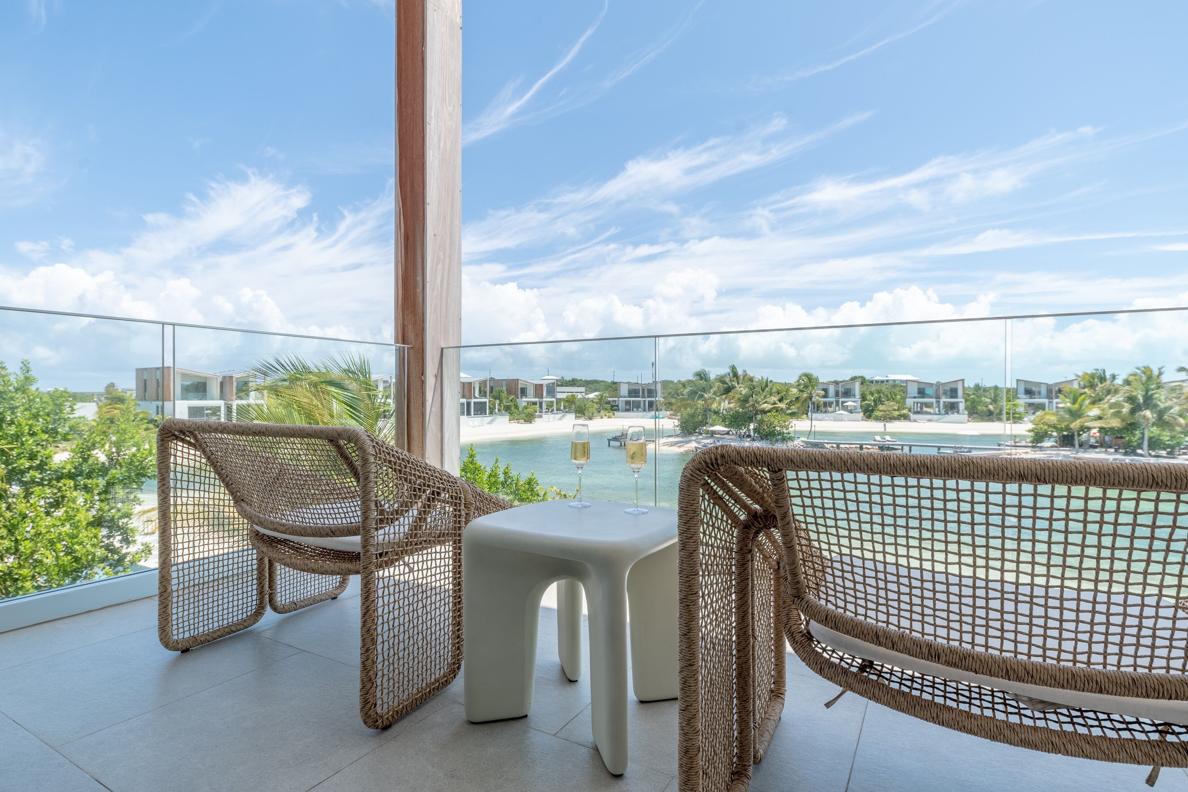 A balcony with wicker furniture and a view of a beach and resort buildings.