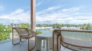 A balcony with wicker furniture and a view of a beach and resort buildings.