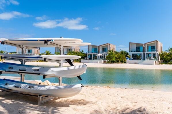 A beach with a row of sea kayaks and a modern resort building with multiple balconies. - Lagoon Villa 5 Bedroom Including Guesthouse LV16 (Providenciales)