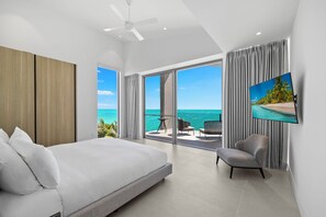 Un dormitorio con una cama grande, televisión, una silla y balcón con vista al océano.