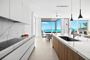 A modern kitchen with a large island, white cabinetry, and a view of the ocean.