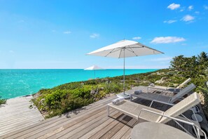 Eine Holzterrasse mit Liegestühlen und Sonnenschirmen mit Blick auf das türkisblaue Meer.