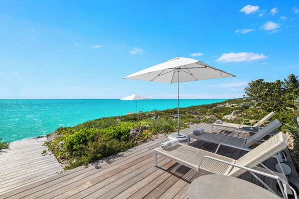 A wooden deck with lounge chairs and umbrellas overlooking a turquoise sea.