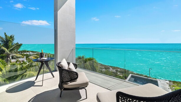 Un balcon avec vue sur l’océan, une table avec des boissons et deux fauteuils en osier.