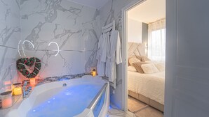 Ein modernes Badezimmer mit Marmorwand, einer herzförmigen Dekoration, einer Badewanne und einem Bett mit Blick.