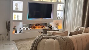 Ein modernes Wohnzimmer mit einem großen Flachbildfernseher an der Wand, einem bequemen Sofa und einem dekorativen Regal mit verschiedenen Gegenständen.