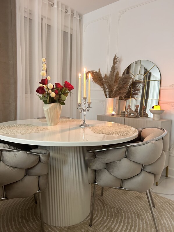 Una mesa redonda de comedor con mantel de encaje blanco, rodeada de sillas grises con capitonado.