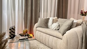 Ein Wohnzimmer mit einem beigefarbenen Sofa, einem Glastisch und einem gemusterten Teppich.