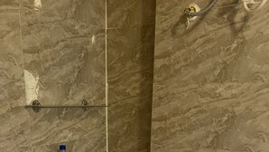 Une salle de bain avec un lavabo sur colonne blanc, une étagère en verre au-dessus du lavabo et un mur en marbre.