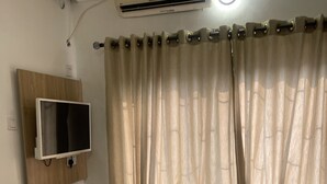 Une chambre à coucher avec un lit, un téléviseur fixé au mur, un climatiseur et des rideaux en voile.