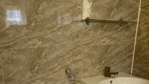 Une salle de bain avec un lavabo sur colonne blanc, une cabine de douche en verre et des murs en marbre.