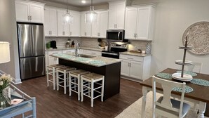 A modern kitchen with white cabinets, stainless steel appliances, a central island with bar stools, and pendant lighting.