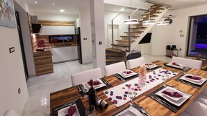 A modern dining area with a wooden table set for a meal, a kitchen in the background, and a staircase leading to another level. - Luxury villa with private pool, sea view (Blaškovici)