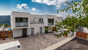 A modern two-story house with a paved driveway, a car parked in the driveway, and a mountain view in the background. - Luxury villa with private pool, sea view (Blaškovici)