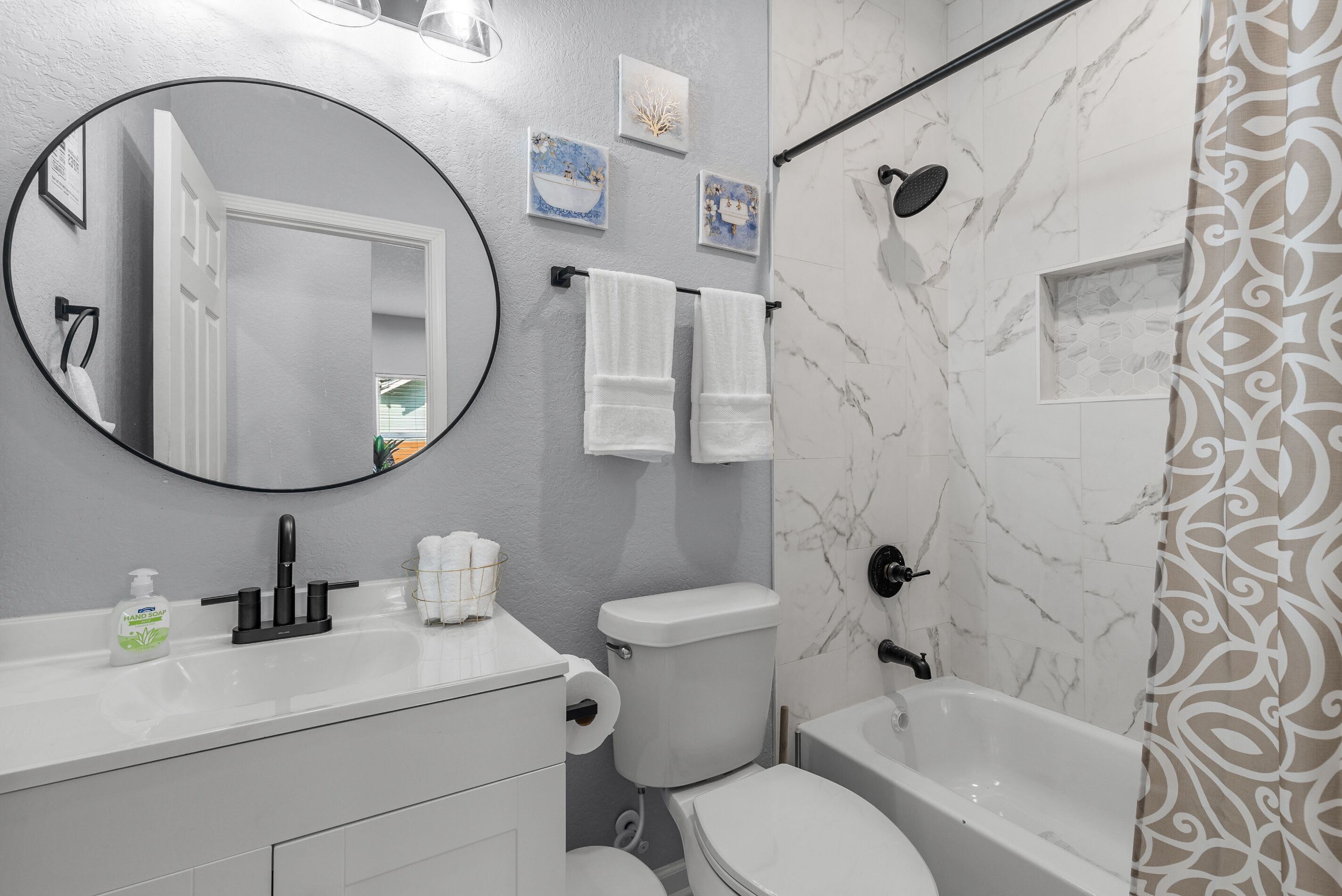 Un baño moderno con un lavamanos blanco, un espejo redondo, un inodoro y una bañera.
