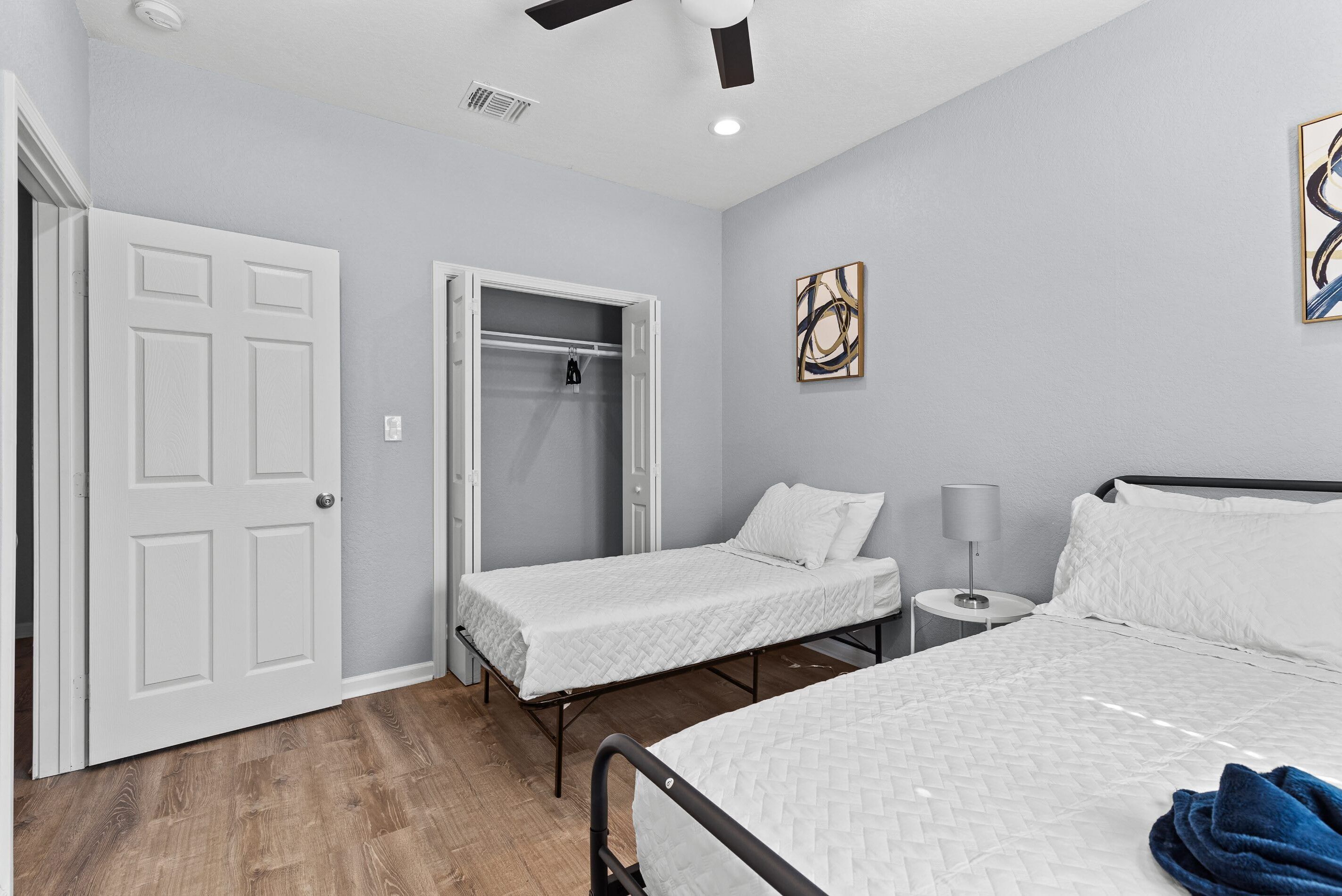 A room with two beds, a closet, a bedside table with a lamp, and a ceiling fan.
