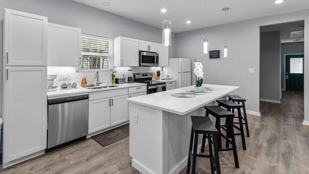 A modern kitchen with white cabinetry, stainless steel appliances, and a central island with bar stools.
