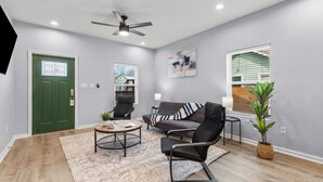 A modern living room with a green door, a ceiling fan, a sofa, a coffee table, and a potted plant.