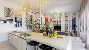 A modern kitchen with a central island, black bar stools, and a staircase leading to a loft area.