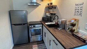 A compact kitchen with a refrigerator, stove, oven, and a wooden countertop.