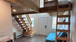 A loft-style bedroom with a bunk bed, a wooden ladder, a staircase, and a small kitchenette area.