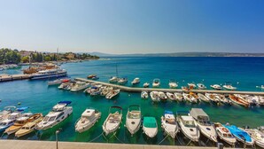 Un port de plaisance où sont amarrés différents types de bateaux, une jetée qui s’avance dans l’eau et, au loin, une côte bordée de bâtiments.