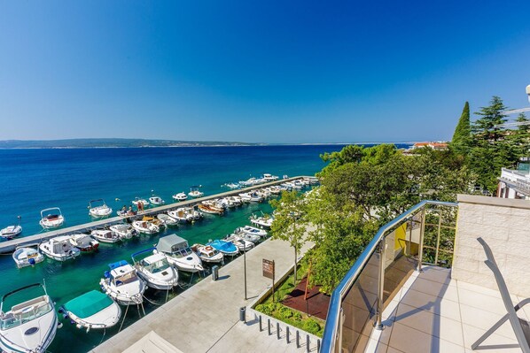 A marina with numerous boats docked, a clear blue sky, and a view of the sea.