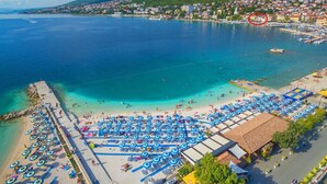 A coastal town with a beach area featuring sun loungers and umbrellas, a pier, and a view of the sea and hills in the background. - Directly by the sea (Selce)