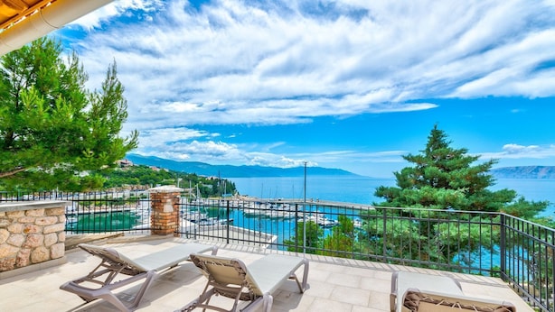 A terrace with three lounge chairs, a stone wall, and a view of a marina and sea. - Luxury with pool, sauna, whirlpool directly by the sea (Novi Vinodolski)