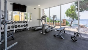 A gym with cardio machines, dumbbells, and a bench. It has large windows with a view of the sea and a balcony with outdoor seating. - Luxury with pool, sauna, whirlpool directly by the sea (Novi Vinodolski)