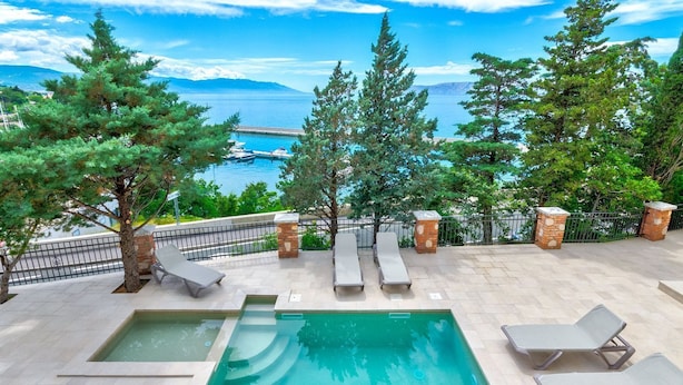Ein Poolbereich mit Liegestühlen und Blick aufs Meer.