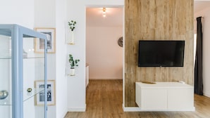Ein modernes Wohnzimmer mit einer Wand als Holzdekor, einem an der Wand befestigten Fernseher und einer Vitrine mit gerahmten Fotos.