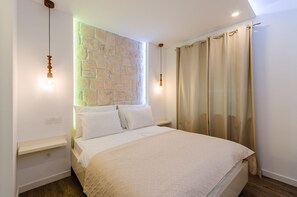 Une chambre avec un mur en pierre, un lit recouvert de draps blancs et deux lampes suspendues.