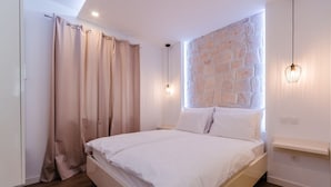 Ein Schlafzimmer mit Bett, Vorhängen, einer Steinwand, einer Hängelampe und Holzboden.