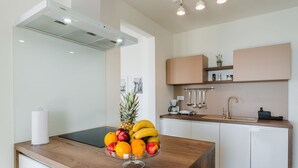 A modern kitchen with a wooden countertop, a fruit bowl, a coffee machine, and white cabinets.