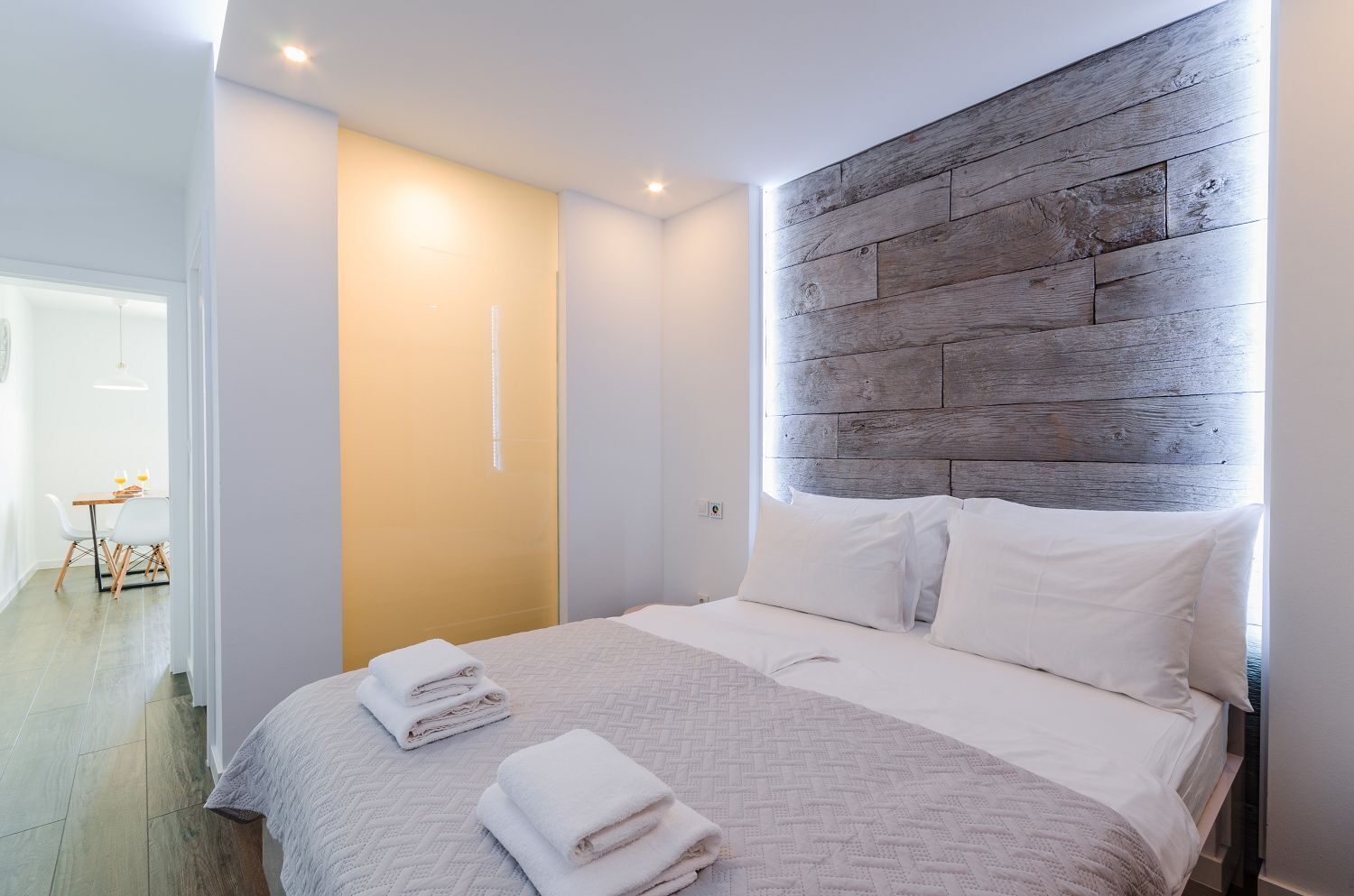 A modern bedroom with a wooden headboard, a neatly made bed, and a bright, well-lit room.